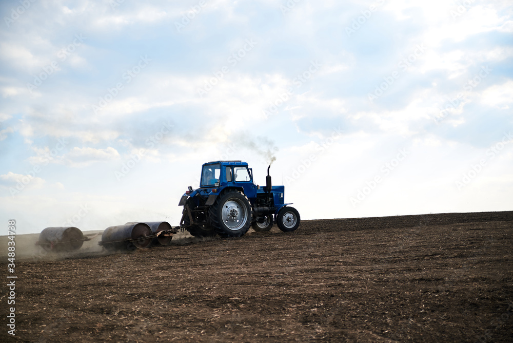 Agricultural work on field with black soil. Blue tractor riding and seeding countryside. Rural works in spring. Environmental protection concept. Ecological products cultivation. Natural background. Agricultural work on field with black soil. Blue tractor riding and seeding countryside. Rural works in spring. Environmental protection concept. Ecological products cultivation. Natural background.