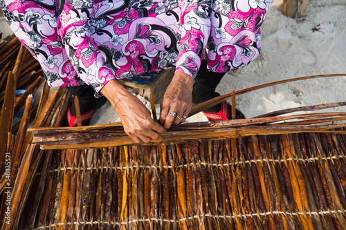 Mani di una vecchia donna alle Maldive impegnate nella tessitura di foglie e rami a costruire tappeti e oggetti d’uso comune