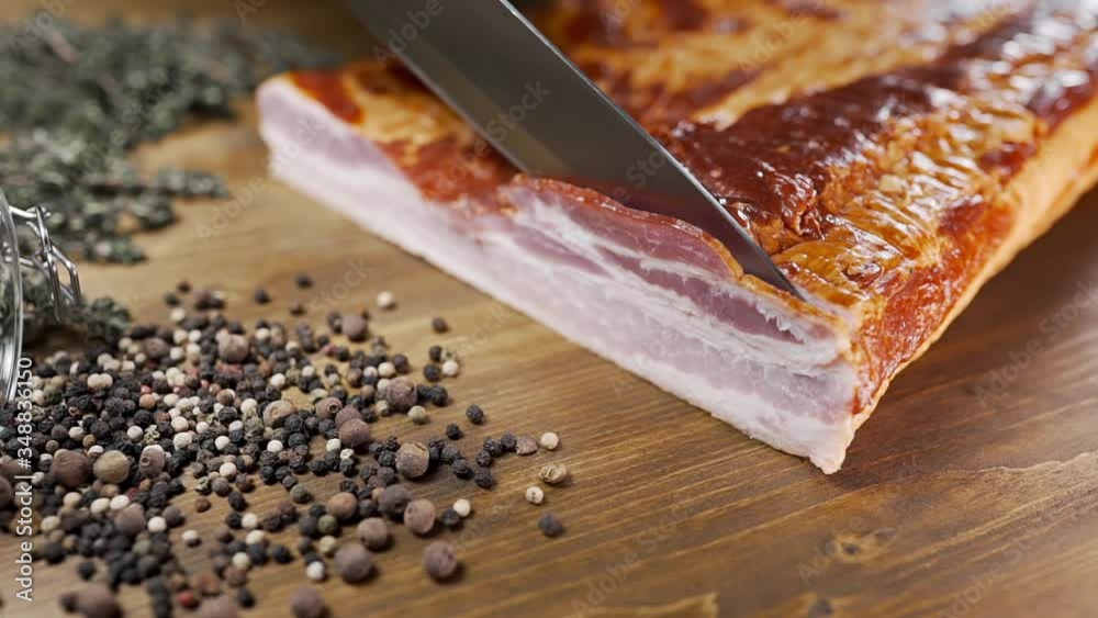 chef cuts pieces of smoked bacon by sharp knife on the wooden board