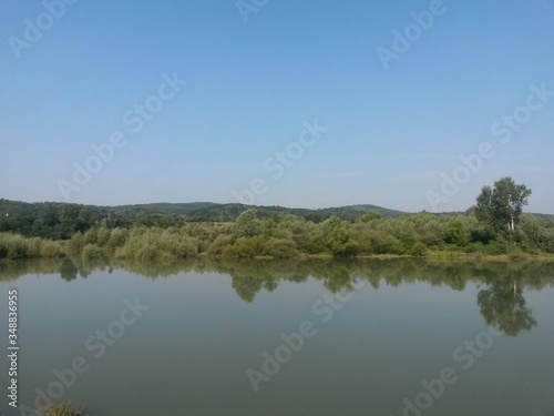 lake reflecting green forest close to the woods in summer season on sunny day with blue sky