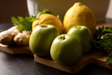 Composition of fruits, still life. Components of Asian cuisine. Lemon with ginger and green apples and herbs on a wooden board and on a dark background