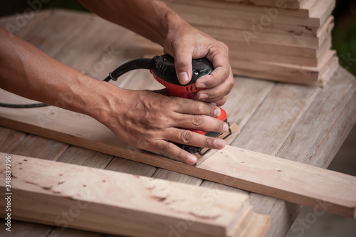 Close up Hands of carpenter equals polishes wooden board with a random orbit sander in the workshop.