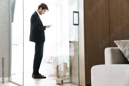 Photo of young brunette businessman using mobile phone while standing