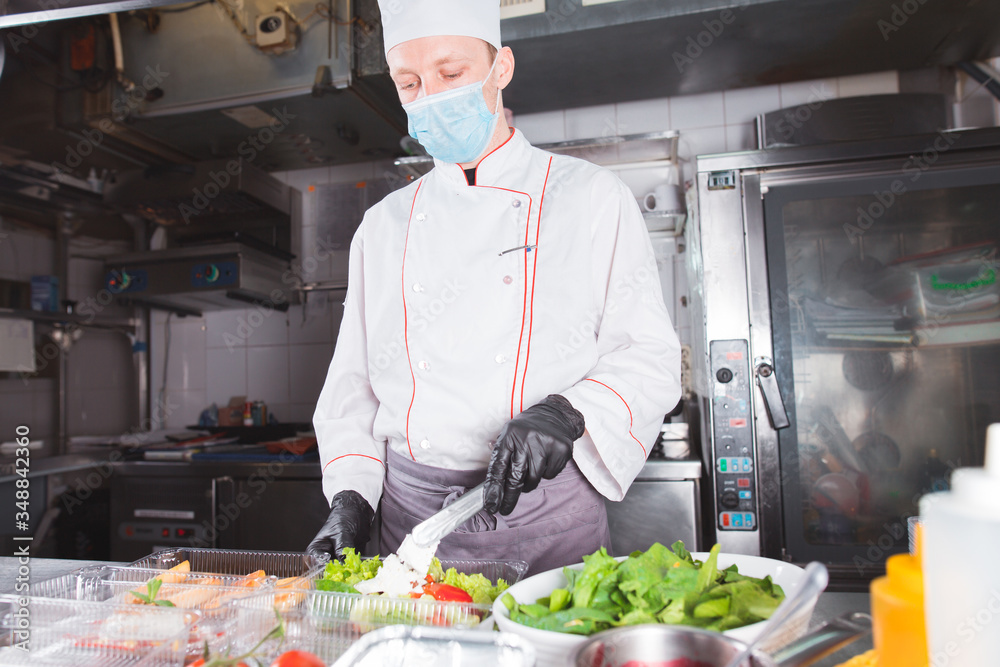 Cooking in a restaurant by a cook in a medical mask and packing in a container Cooking in a restaurant by a cook in a medical mask and packing in a container