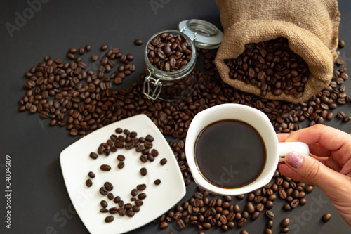 a woman holds a Cup of coffee over scattered coffee beans on a black background