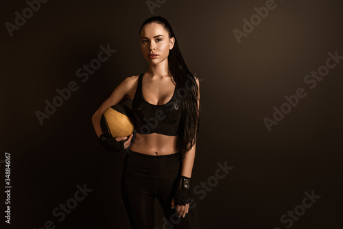Brunette sportswoman with ball looking at camera isolated on black