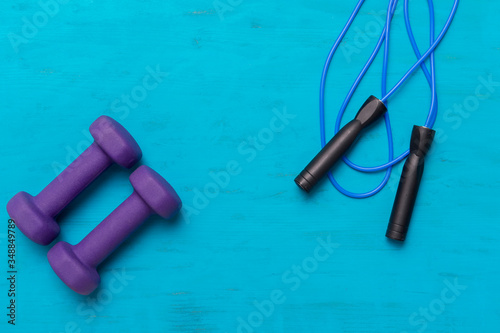 Jumping rope and dumbbells on blue wooden background. Workout online concept.