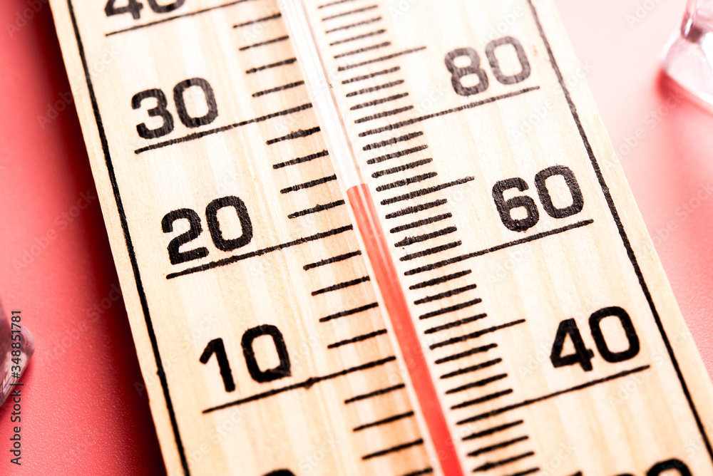 Wood thermometer shows high temperatures in fahrenheit or celsius on light pink background with ice cubes. Wood thermometer shows high temperatures in fahrenheit or celsius on light pink background with ice cubes.