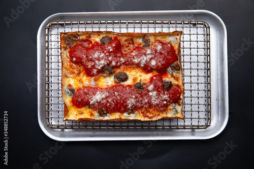 detroit pizza on an iron tray on a dark background. selective focus