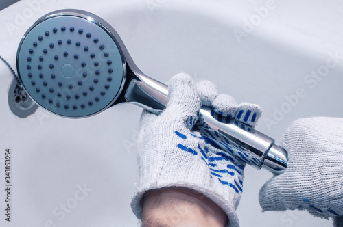 Repairman mounts a shower hose. Close-up of gloved hands. Cold blue tint