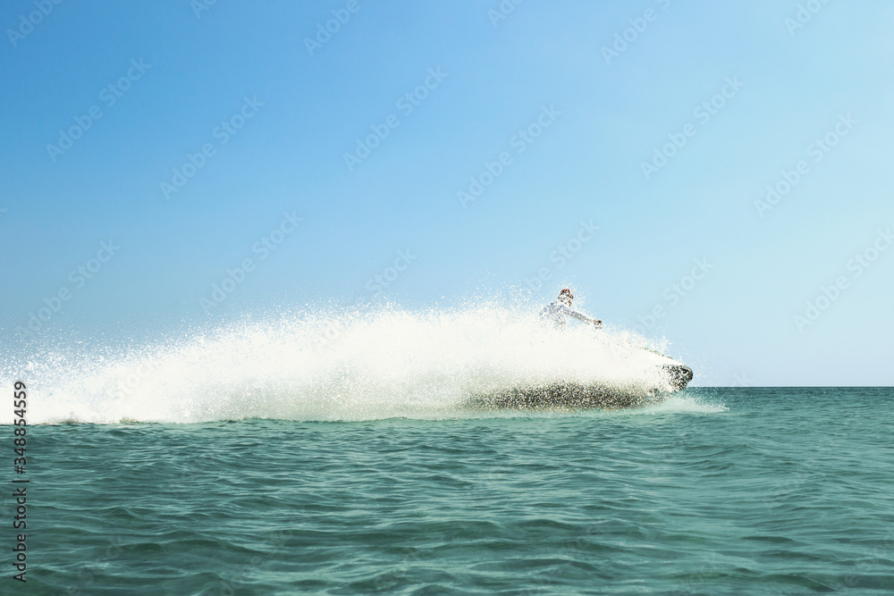 Obraz premium Vacation at sea in hot Sunny weather, A person on a jet ski rides on the sea water very fast with splashes around it against the blue sky, rest in the fresh sea air, travel by sea