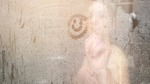 blurry naked lady draws smile on white steam condensate on glass-enclosed shower door in bathroom at home close view