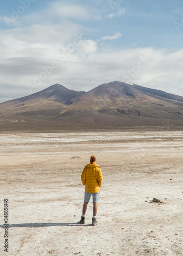 Tourist Man. Dry, barren landscape mountain background. Dramatic desert, snowcapped mountains wilderness. Mountain range view. Salt Flats of Uyuni, Bolivia. Blue sky, nature, hiking, and sand dust