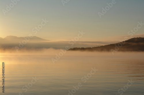A scenic landscape - morning fog over the calm water of Chivyrkuisky Bay. Golden sunrise in a Zmeyevaya Bay  peninsula Svyatoy Nos  Holy Nose peninsula   Baikal Lake  Siberia  Russia