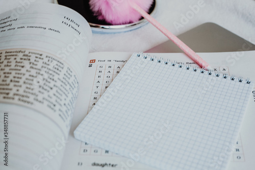 on the table there is an open English-language textbook, a table lamp, an open notebook in a cage, an educational process, homework, for students, a light background, stay at home, a pink fluffy pen f