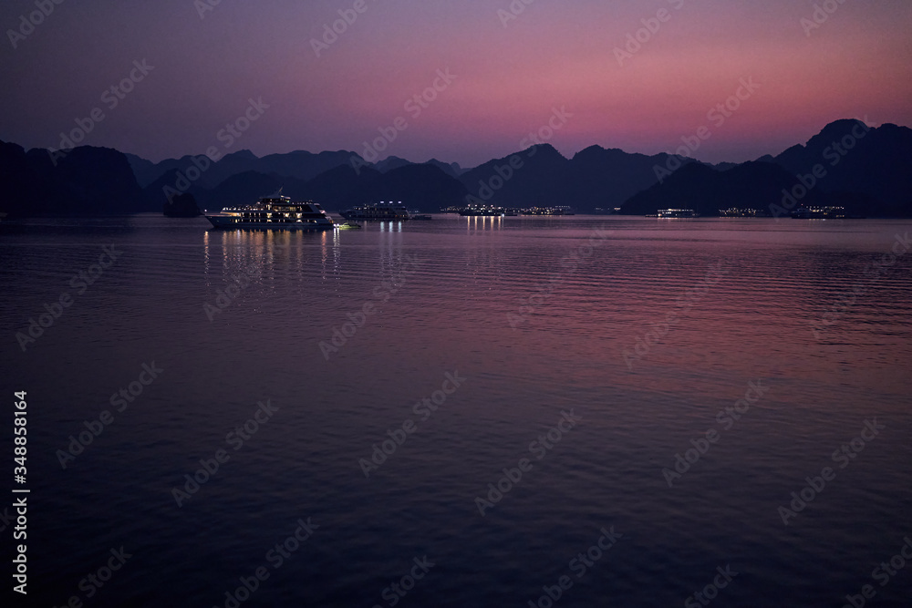 Breath-taking sunset with luxury cruise ships between the rock formations at the Ha Long Bay,