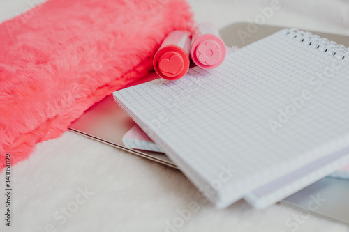 on a white table there is an open notebook in a cage and two markers of pink and red, for notes, the educational process, next to a fluffy red notebook, stay home

