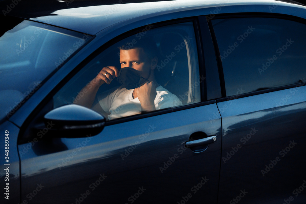 Attractive man driver in medical face mask inside the grey car, concept of coronavirus quarantine