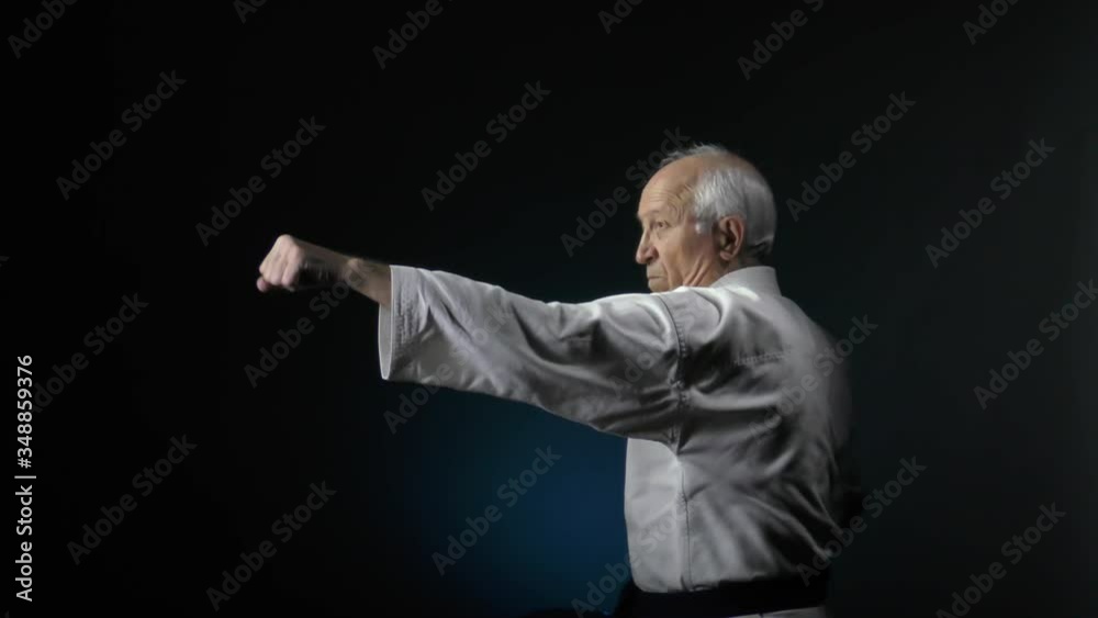 Formal exercises karate old man athlete trains against a dark background Formal exercises karate old man athlete trains against a dark background