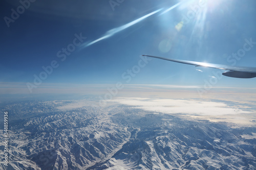 boundless fantastic mountains range under rare white clouds against vast blue sky view from airplane window
