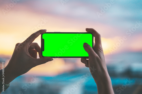 Fotografie Pair of hands holding a smartphone on a green screen