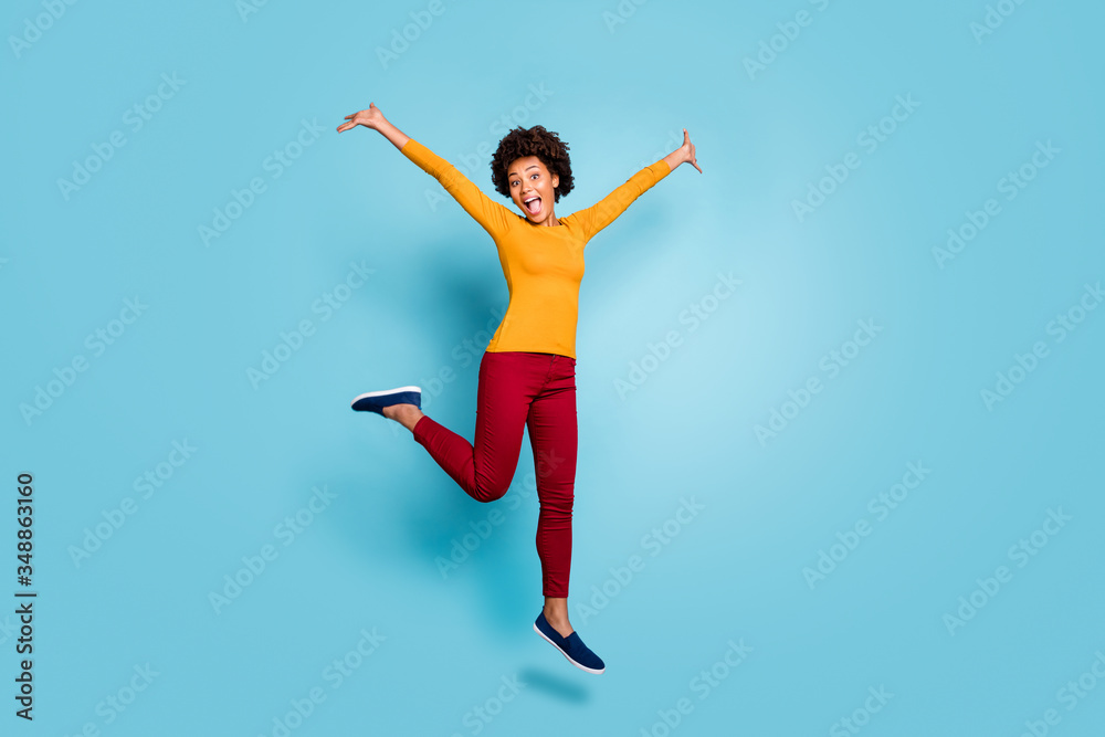 Full length photo of funny dark skin lady jumping up high rejoicing spend vacation abroad addicted shopper wear yellow shirt red pants footwear isolated blue color background