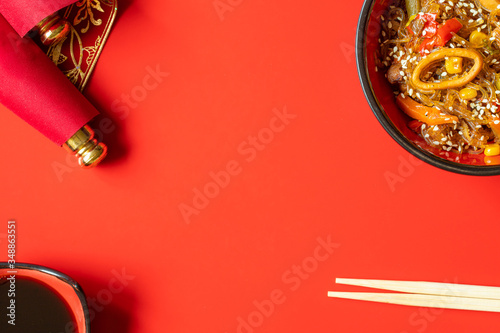 noodles with seafood and vegetables, chopsticks, soy sauce on red background. menu design template with copy space 