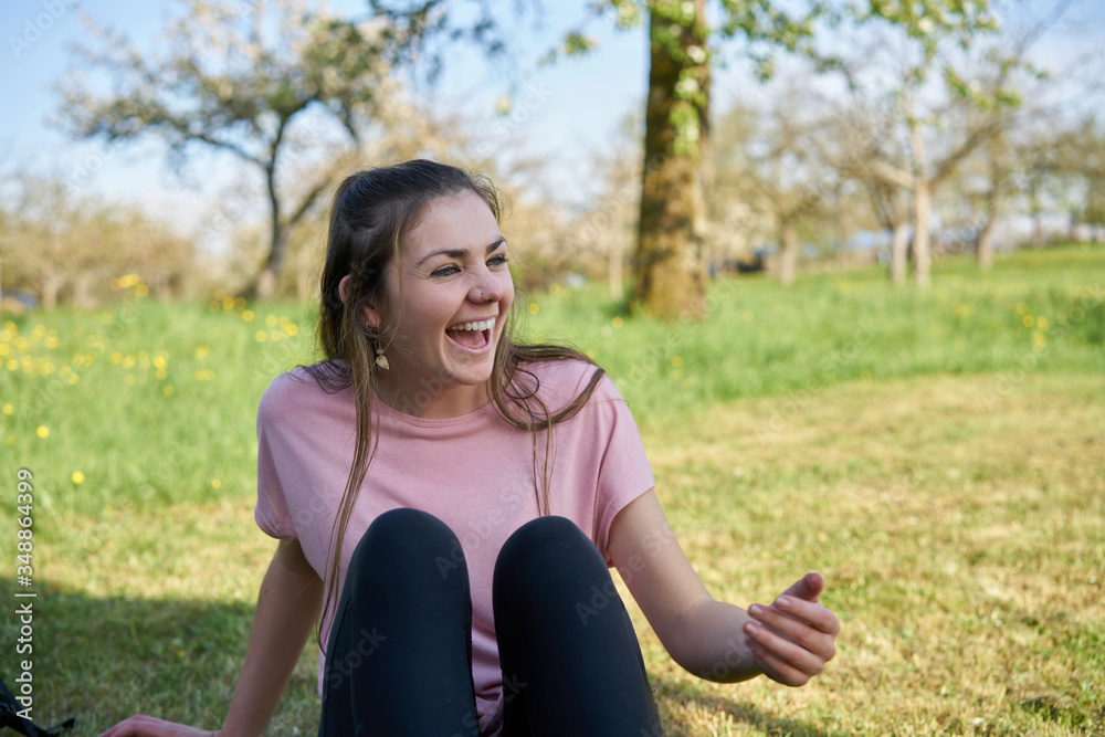 Young woman sitting in a meadow in spring laughing and having lots of fun in the background fruit trees Young woman sitting in a meadow in spring laughing and having lots of fun in the background fruit trees