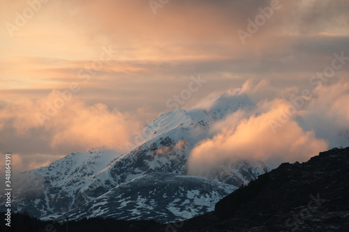 peaks of norway. sunset over mountains in lofoten islands. north of norway. Orange clouds around snowy mountains during amazing sunset from distance 