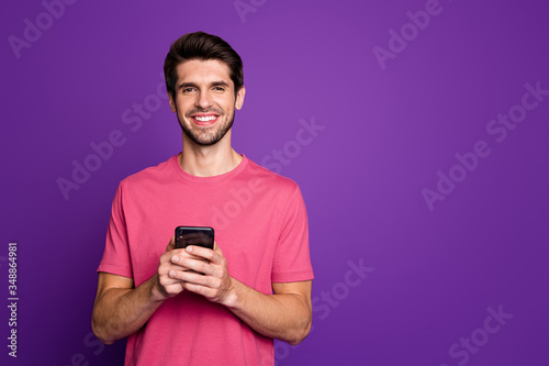 Photo of handsome attractive guy young millennial hold telephone hands popular blogger addicted user wear casual pink t-shirt isolated purple color background © deagreez