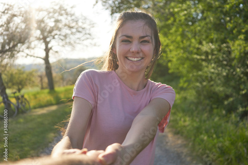 Young happy smiling woman in a pink shirt dancing around in nature, in the background a meadow, bushes and a bicycle