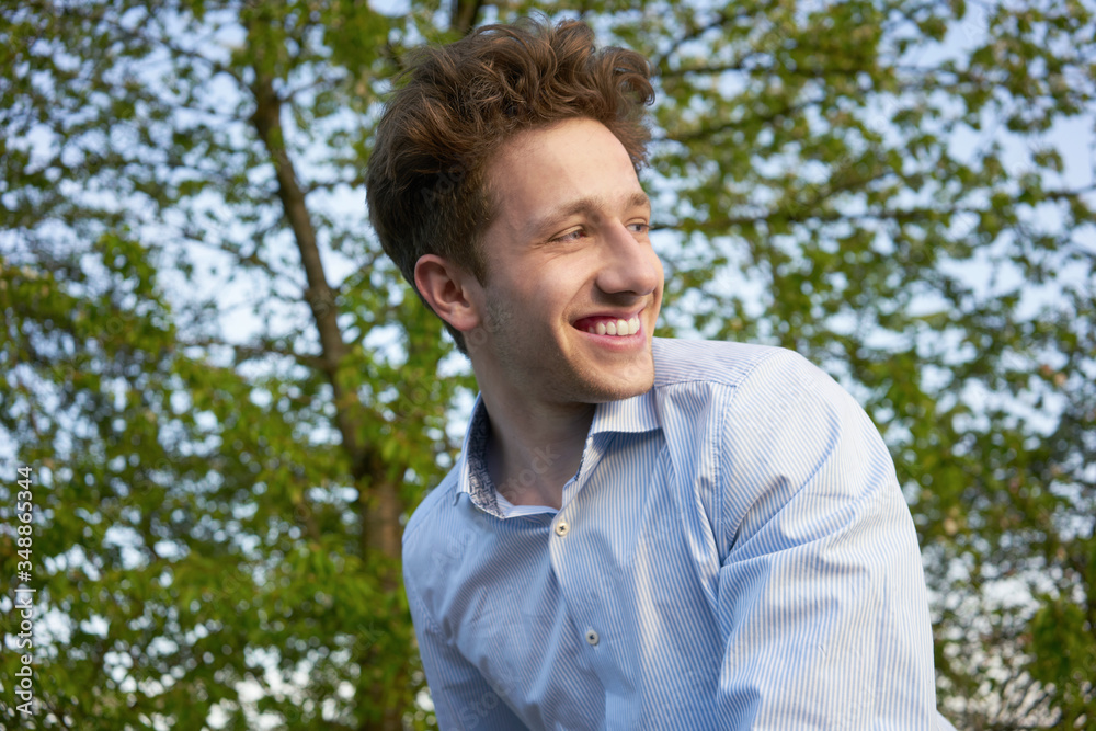 Portrait of a young handsome happily laughing man looking over his shoulder in beautiful greenery Portrait of a young handsome happily laughing man looking over his shoulder in beautiful greenery