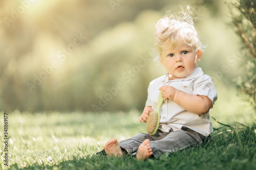 Cute little baby boy sitting on the grass in summer, on a Sunny day. Selective focus, space for text