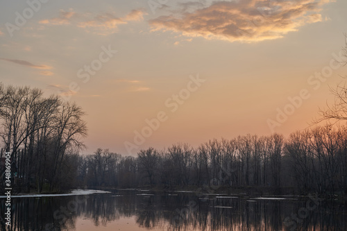    Early spring. Morning dawn over the lake in a misty, thoughtful haze. Beautiful view of the forest covered with fog early in the morning. The sun's rays of light.       