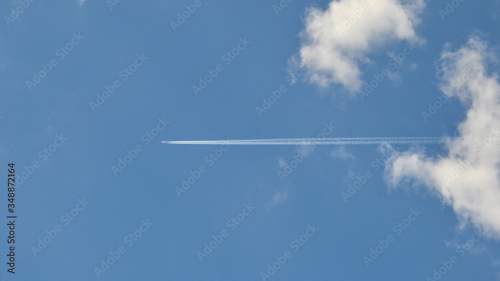 Trace of an airplane in the blue sky. Jet airplane leaves contrails (or vapor trails, traces) on blue sky background. Travel, holidays, vacation concept Trace of an airplane in the blue sky. Jet airplane leaves contrails (or vapor trails, traces) on blue sky background. Travel, holidays, vacation concept