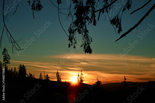Sunrise/sunset with bloody sun in the middle and deep blue sky with forest silhouette in the foreground.