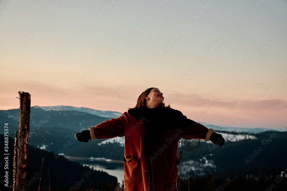 Beautiful young woman looking at the sky with her arms in the air at golden hour with beautiful scenery in the background. 