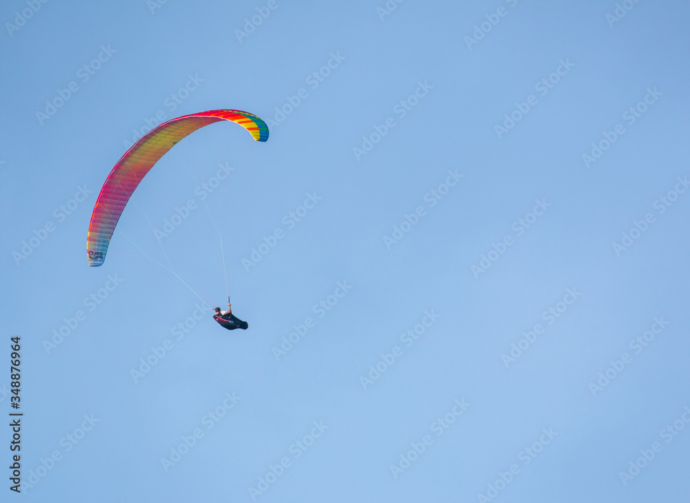 Orange and yellow paraglider on clear blue sky Orange and yellow paraglider on clear blue sky