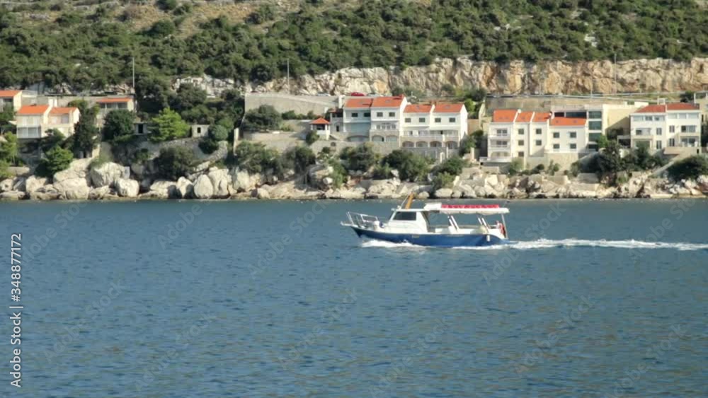 Small boat sailing by with red roofed, ocean cliff side buildings behind in Croatia. Small boat sailing by with red roofed, ocean cliff side buildings behind in Croatia.