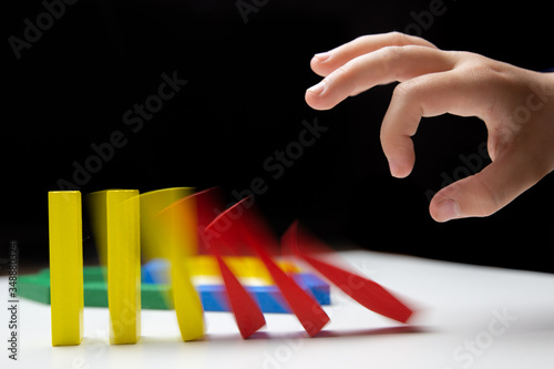 Domino effect. Domino of colorful wooden blocks. Children's hand pushes dominoes on a white table. Motion effect