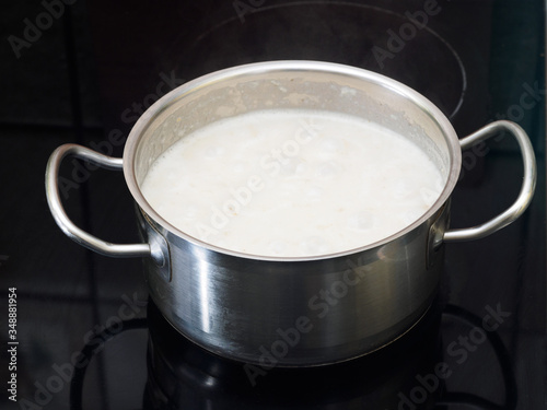 Stainless steel pan with boiling oatmeal on the stove. Cooking concept