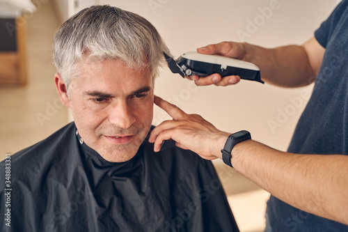 Adult person makes haircut to elderly man