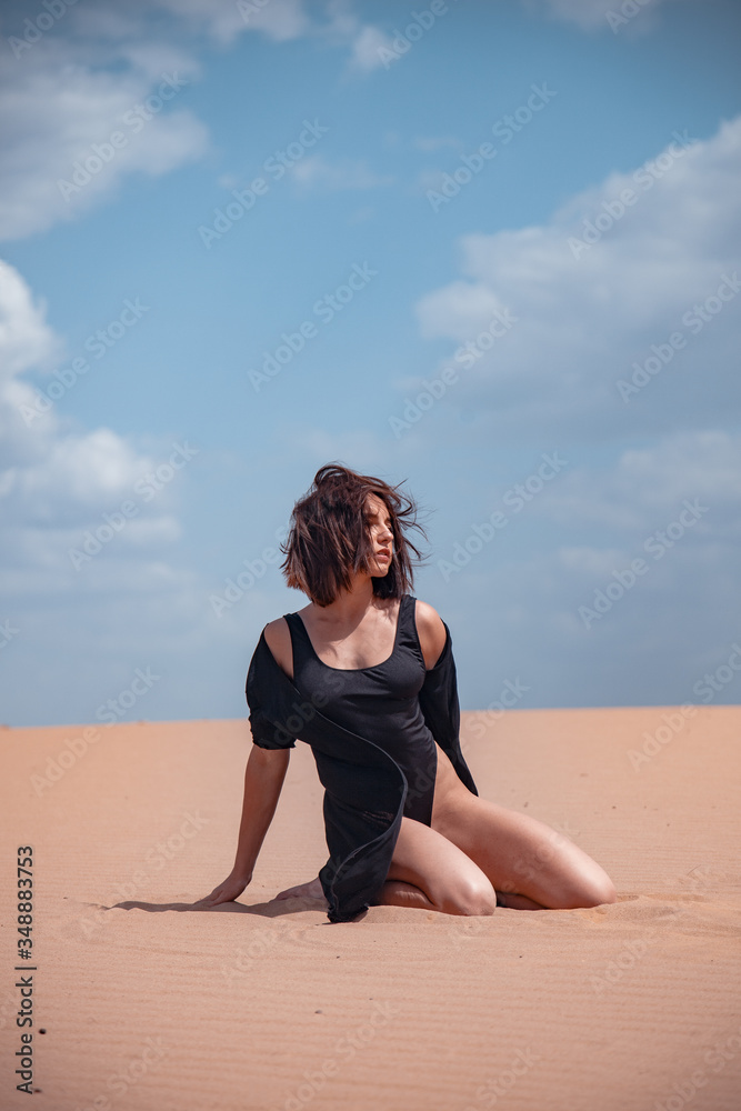 A girl in a black swimsuit sits on the sand in the desert