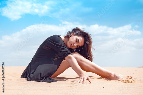A girl in a black swimsuit sits on the sand in the desert