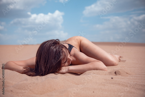 The girl in a black piece swimsuit lies on the sand in the desert