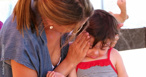 Mom applying sunscreen to upset child feeling angr photo