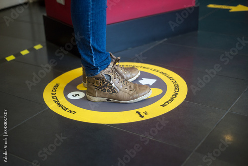 Closeup of feet of woman standing in the social distancing symbol on the floor in the train station  during the Covid-19 pandemic