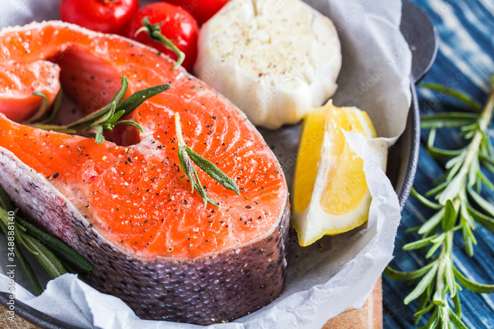fresh raw salmon steak with rosemary, lemon and spices in a black pan on a blue rustic background. Balanced diet or cooking concept. fresh raw salmon steak with rosemary, lemon and spices in a black pan on a blue rustic background. Balanced diet or cooking concept.