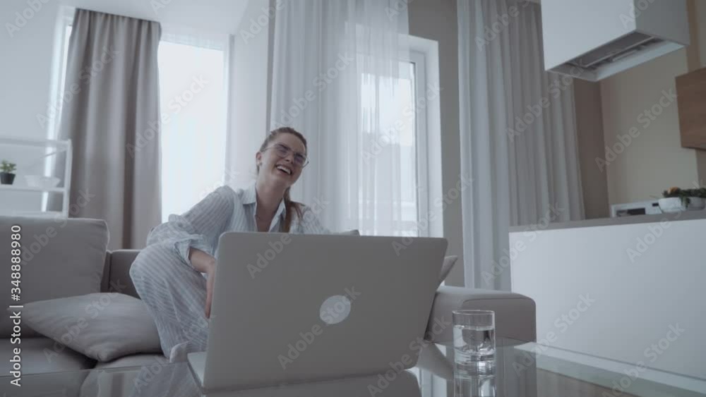 Happy smiling woman sitting on sofa and using laptop at home, looking at screen and laughs, watching funny video Happy smiling woman sitting on sofa and using laptop at home, looking at screen and laughs, watching funny video