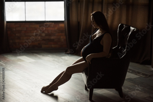 Pregnant women, photoshoot in dark key sit on the armchair  © alexash